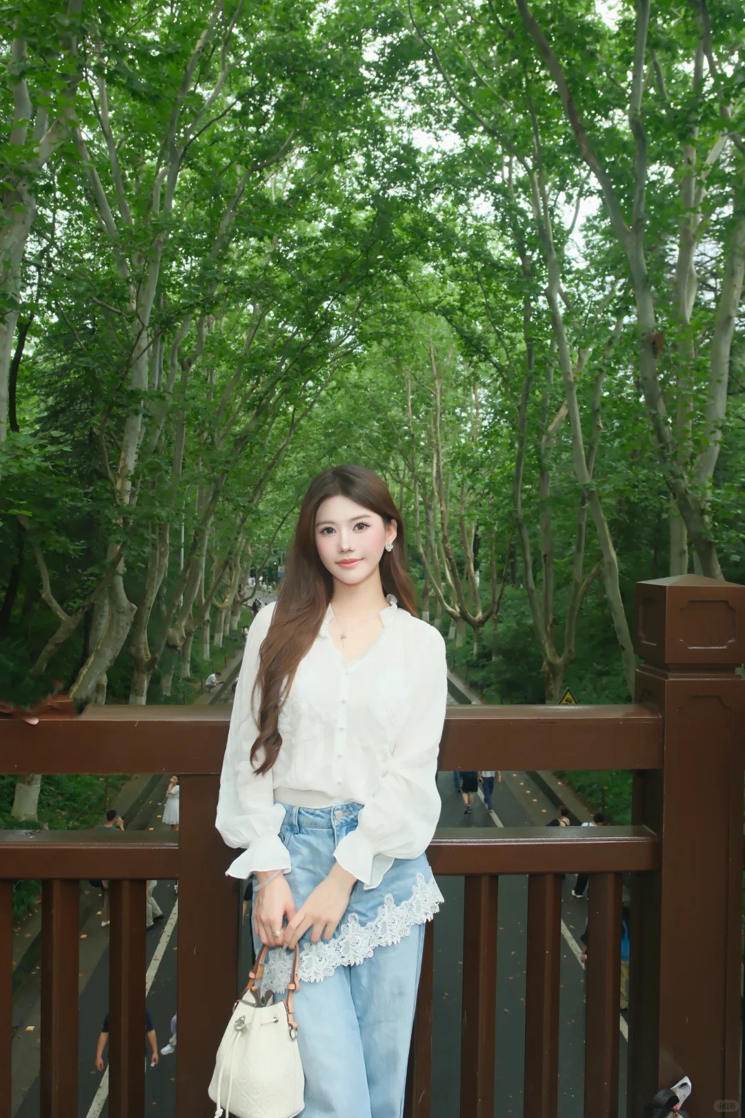 穿浅色上衣和牛仔裤的女性站在绿树旁